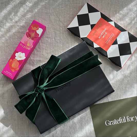 Black gift box with a green ribbon, a pink and white floral package, and a black and white checkered box on a textured surface.